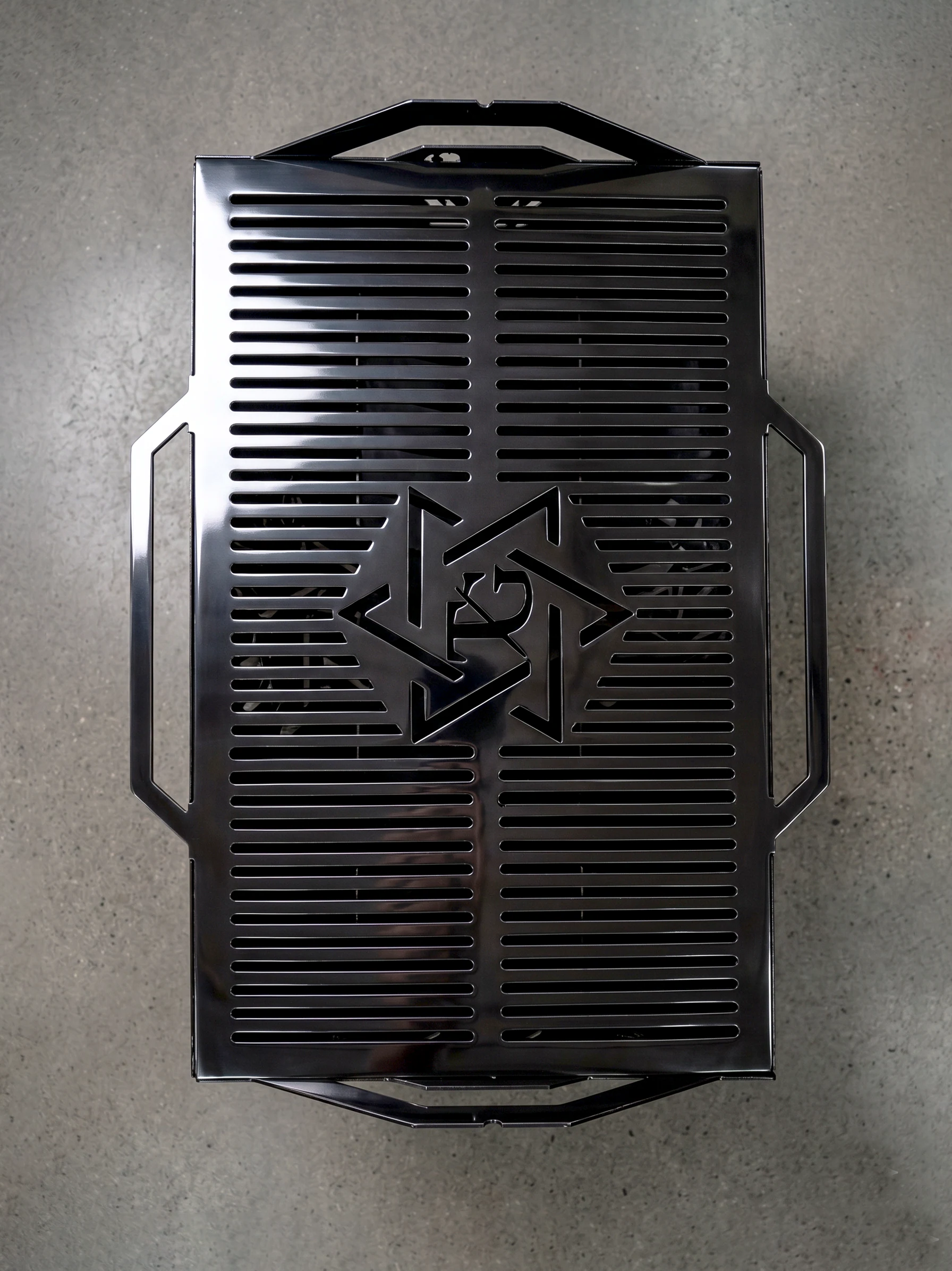 Asador de acero negro con tapa de ranuras y un diseño geométrico cortado en plasma, visto desde arriba